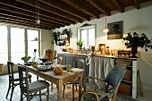 Einfache Küchenzeile mit Vorhang und Aufbewahrungskörben unter kleinem Sprossenfenster in traulicher Landhausküche mit rustikalem Holztisch und Vintage-Stühlen