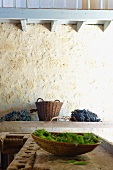 Schale mit Blättern auf einer Hobelbank und Weinbeeren vor historischer Sandsteinmauer (Château Maignaut)