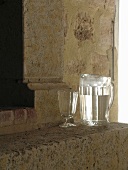 Wasserkrug und Kelchglas vor dem Kamin in historischem Sandsteingemäuer