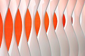 Detail of wall element made from separate, shaped blades in front of orange wall