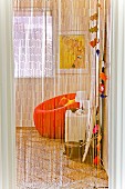 View through airy fringe curtain to colorful corner of room with orange armchair