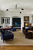 Art deco armchairs with royal blue covers and black frames below multiple-armed ceiling lamp in grand living room