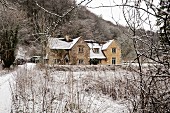 Blick durch kahle Zweige auf die Backsteinfassade eines englischen Landhauses in verschneiter Winterlandschaft
