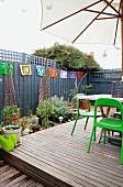 Roof terrace with wooden platform, garden furniture and parasol surrounded by screen and various potted plants