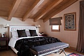 Upholstered bench at foot of double bed in attic room with wood-beamed ceiling