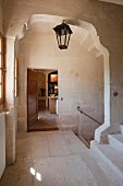 Staircase landing with walls and floor of pale stone; dark, lantern-style lamp in middle