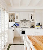 weiße Einbauküche im romantischen Landhausstil mit weißer Holzbalkendecke