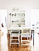 Dining table and vintage chairs in front of open shelves of crockery