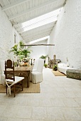 Grosszügige Loggia eines mediterranen Wohnhauses in Weiß mit Hussenstühlen und antikem Stuhl vor rustikalem Tisch