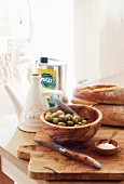 Oliven, Olivenöl, Brot, Salz & Taschenmesser auf Holzbrett in Küche des Château Maignaut (Pyrenäen, Frankreich)