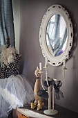 Candelabra and ornaments on chest of drawers below wall-mounted mirror