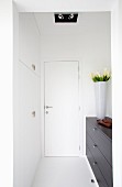 Vase of flowers on dark chest of drawers in white, contemporary foyer