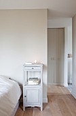 Lit candle lantern and stacked books on vintage bedside cabinet against pastel wall next to double bed