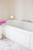 Bathtub in pale bathroom in natural shades with stone floor; two pink towels provide a cheerful splash of colour