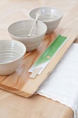 Pale grey clay bowls and chopsticks wrapped in paper on wooden board