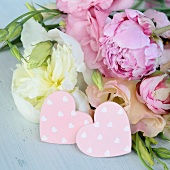 Zwei rosa Dekoherzen vor Blumenstrauss (Pfingstrosen)