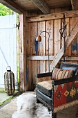 Old leather armchair with combination of fabrics in front of open door of wooden cabin
