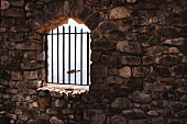 Barred, arched window opening in stone wall