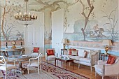 Period furniture in stately home salon - upholstered chairs around round, solid wooden table and console table against wall painted with mythological motifs