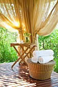Sunny spa area with rattan table and stool; rolled white towels on stool
