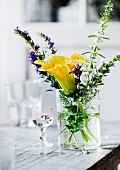 Yellow courgette flower and flowering herbs in glass of water on old table