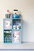 Decorative idea for simple shelf: floral fabric, cups, flowers in glass bottles and old picture frames create a whole new look