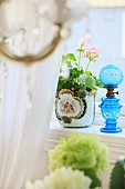 Blue glass oil lamp next to potted geranium on windowsill