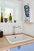 Kitchen sink and blue and white china plates in plate rack on white wooden wall