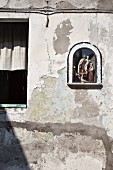 Kleine Nische mit religiösen Figuren in verwitterter Hausfassade