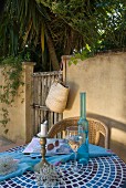 Weinglas und Flasche auf gefliestem Tisch vor Gartenmauer
