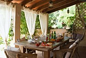 A table laid for a meal, with rattan chairs, on the veranda