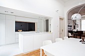 Einbauküche und Esstisch mit Designerstühlen im puristisch weiss gestalteten, offenen Wohn/Essraum einer schicken Altbauwohnung