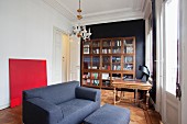 Blue two-seater sofa in front of bright red painting and bookcase in study of grand period apartment