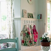 Floral fabric bags hanging from ornamental coat rack on wood-panelled wall in rustic kitchen-dining room