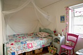 Romantic, country-house bed with patchwork quilt and draped mosquito net in child's bedroom