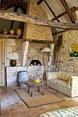 Side table and sofa in front of wood-fired bread oven and stone walls in rustic interior