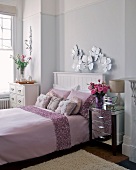 Double bed with pale pink bedspread, silver bedside table and white chest of drawers in elegant bedroom
