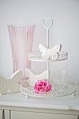 Glass of water, pink rose and butterfly ornaments on cake stand