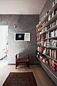 Antique stool and Oriental rug in front of grey marbled wall; letter ornaments on narrow, floating bookshelves to one side