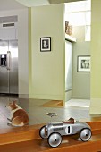 Vintage children's vehicle on stair and dog on floor in a modern entrance hall with open kitchen area and look in the next room