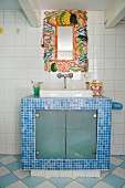 Spiegelrahmen mit Gemüsemotiven über gemauertem Waschtisch mit blauen Mosaikfliesen
