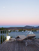 Twilight atmosphere on roof terrace with view of mountain landscape - dog on wooden floor next to sun lounger