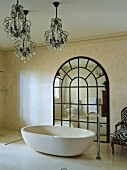 Free-standing, designer bathtub with standpipe tap fitting and chandeliers in front of large, arched lattice mirror