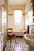 Blick durch offene Tür auf antiken Holzstuhl und gemusterten Fliesenboden im Vintage Bad