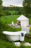 Vintage bathtub on mountain slope and view of tent-like pavilion in green meadow