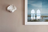 Shell-shaped sconce lamp next to framed picture with reflection in glass on pale grey wall