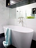 Free-standing designer bathtub with retro tap fittings; dark wood bathroom cabinet above wall-mounted mirror