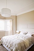 Double bed with elegant bedspread and simple pendant lamp with white lampshade in beige-painted bedroom with traditional ambiance