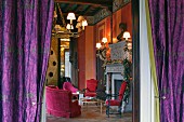 View through purple curtains into flamboyant Renaissance salon with red upholstered seating in front of fireplace