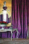 Rococo table in front of purple, patterned curtain and illustration of woman in dress of same fabric